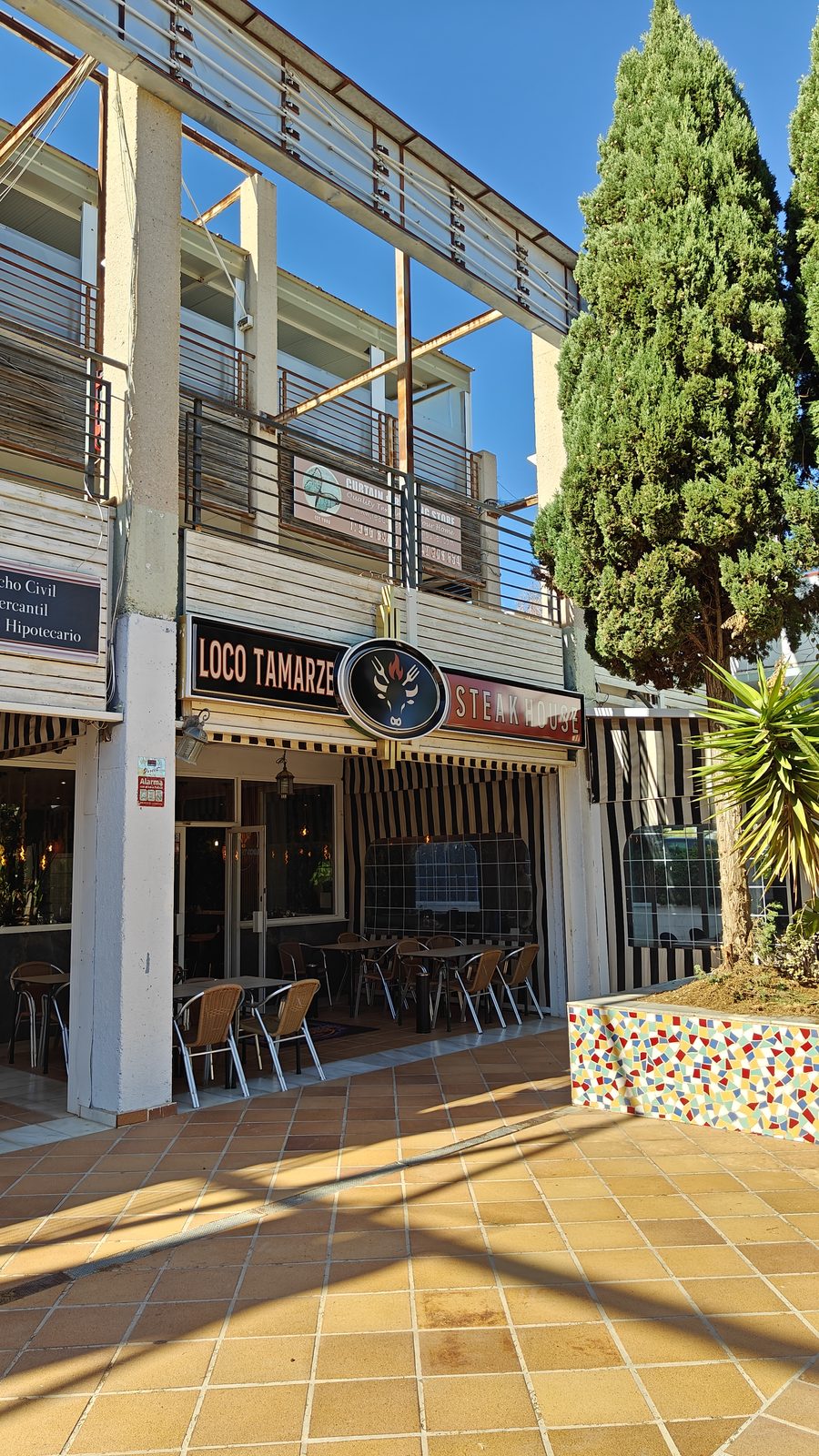 Restaurant terrace beneath an upper-floor walkway in Los Dolses